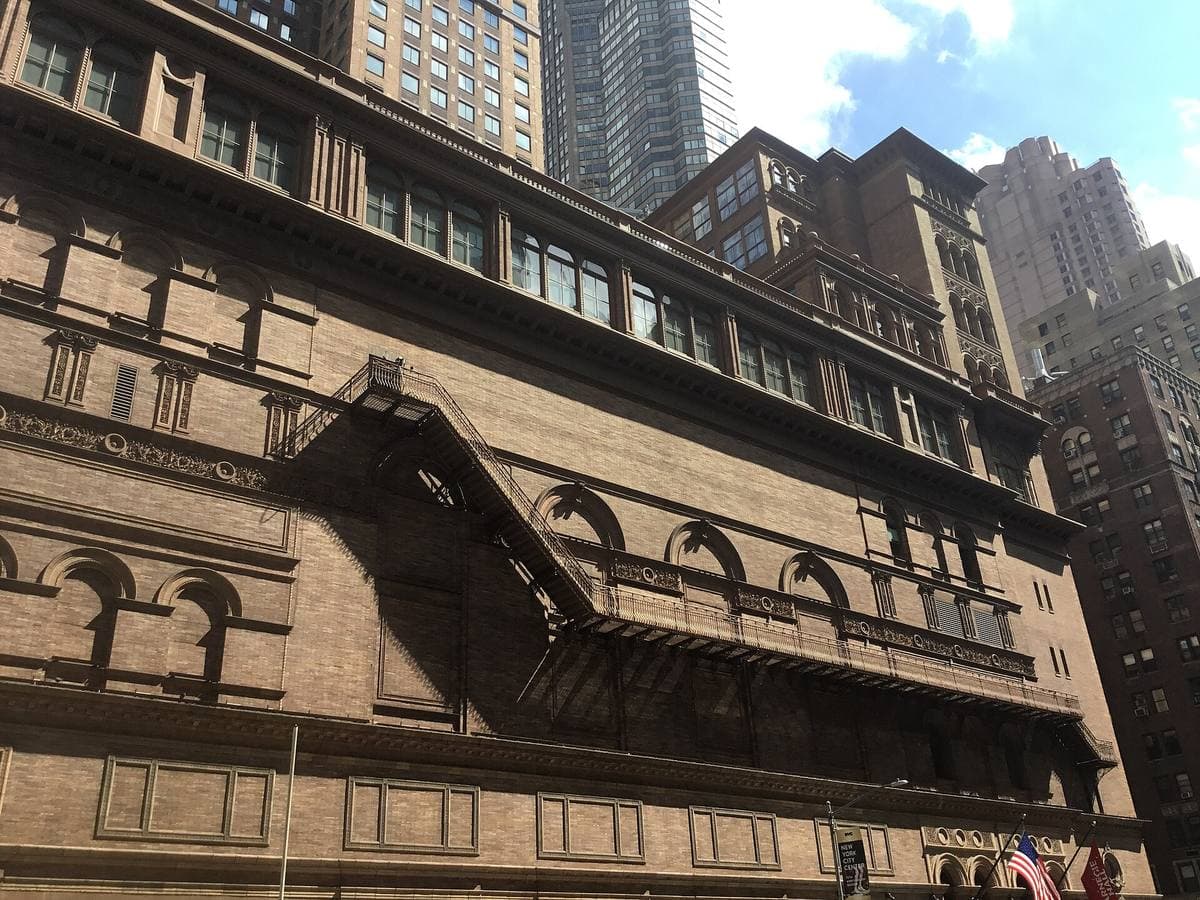 The brown-brick front of Carnegie Hall with arched windows and flags
