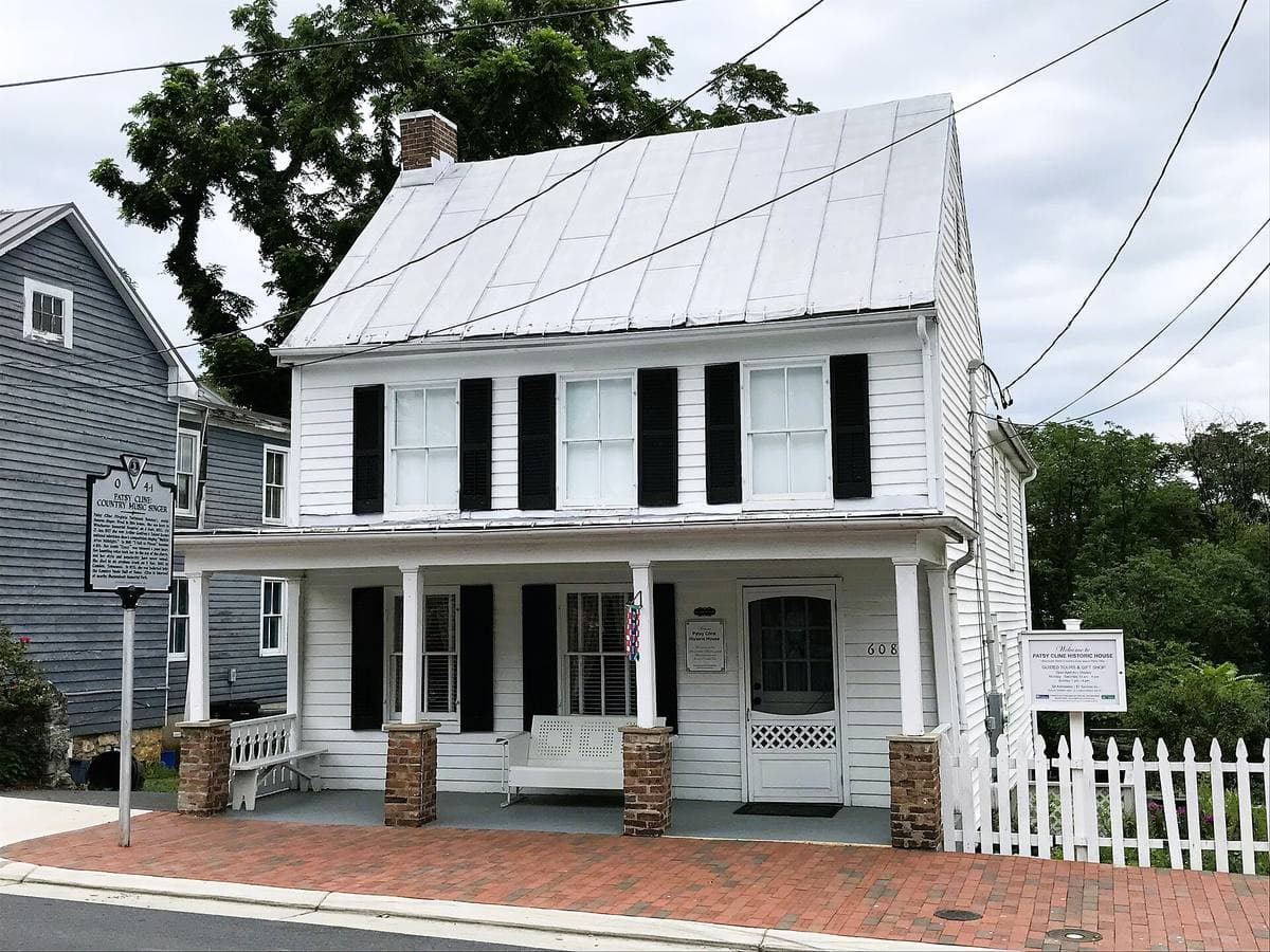A white two-storey clapboard house with black shutters, a porch and a picket fence