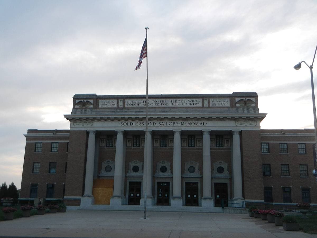 A pale stone civic hall with a row of columns across its front and a flag above