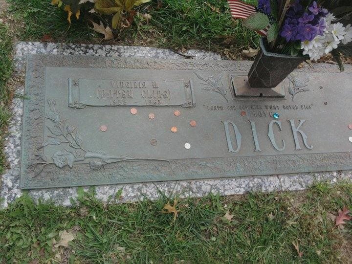 A bronze grave plaque in the grass with coins laid along its edge and flowers above