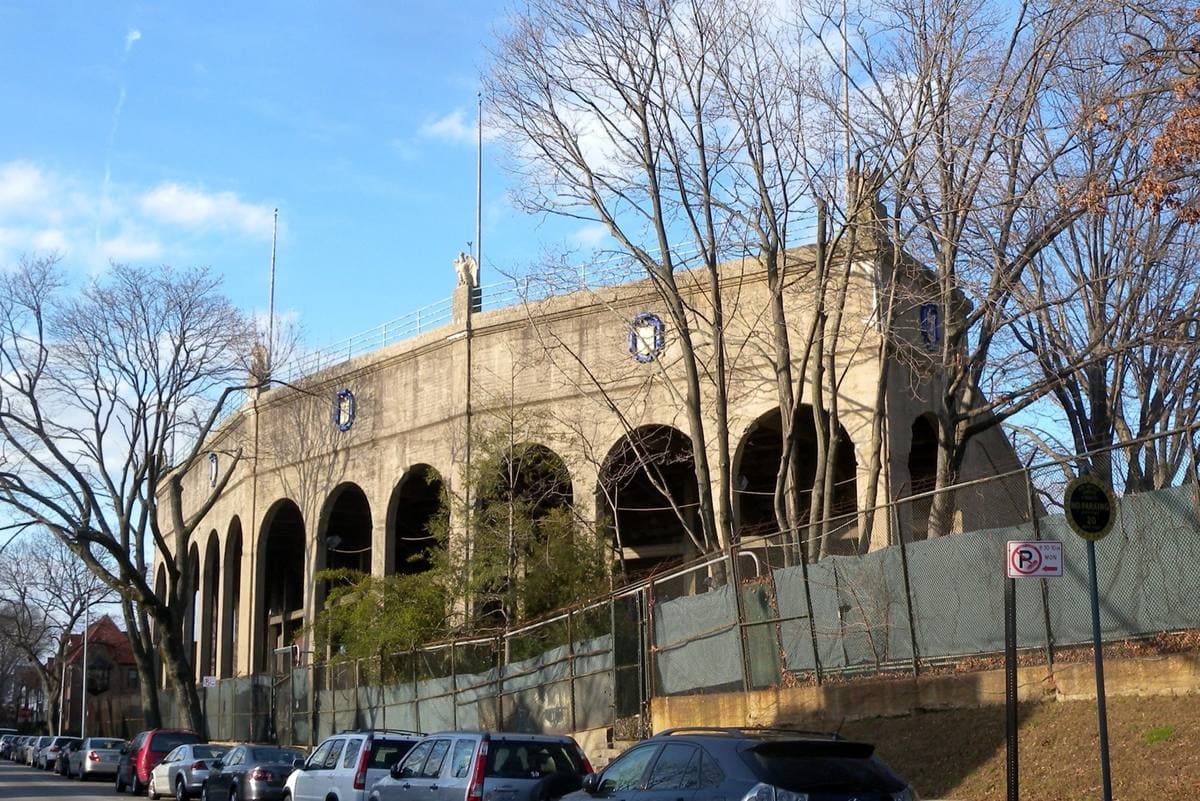 The arched concrete outer wall of a 1920s stadium behind bare trees