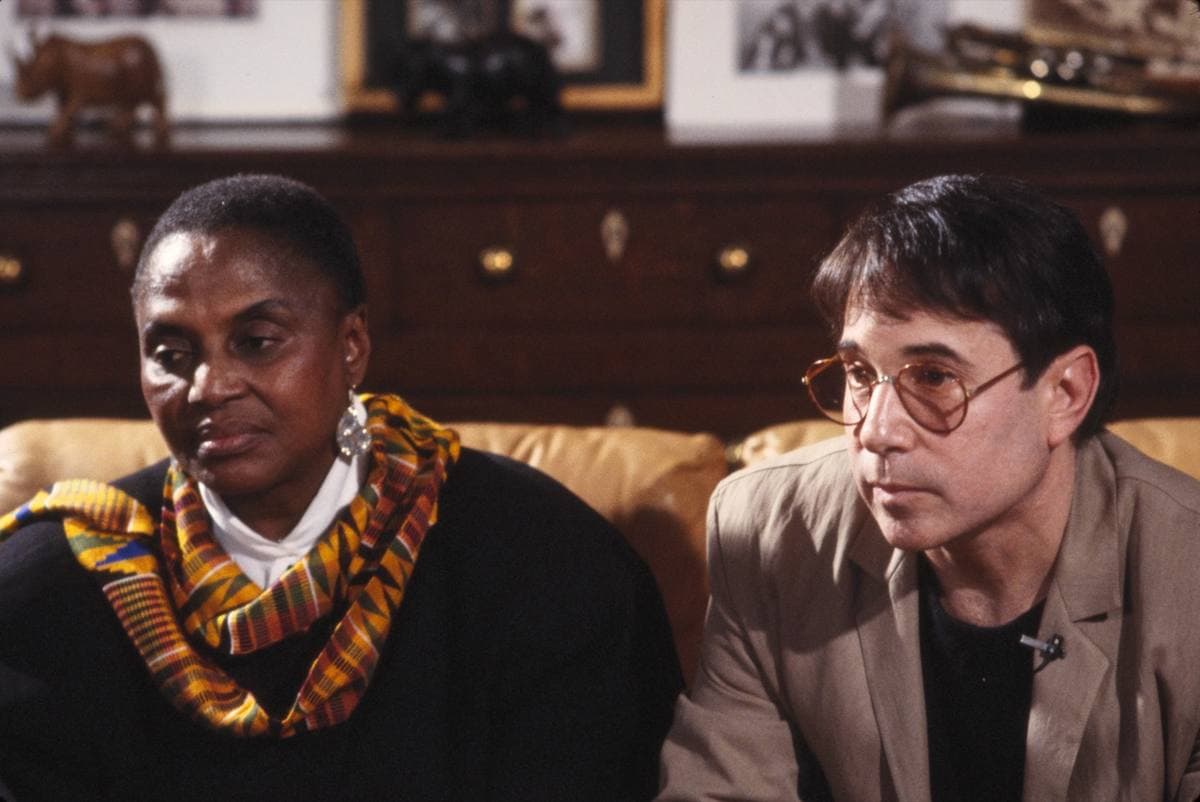 Miriam Makeba in a patterned scarf beside Paul Simon in glasses and a jacket