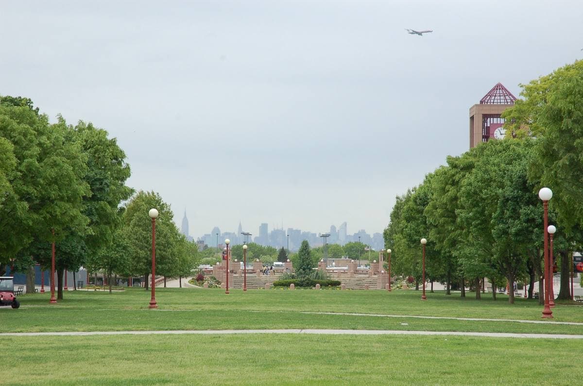A wide college lawn lined with trees and lamps, the Manhattan skyline far off