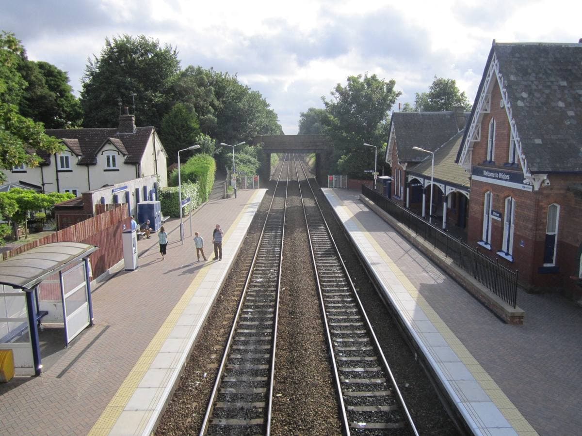 Two platforms either side of the tracks at a small red-brick station with a footbridge