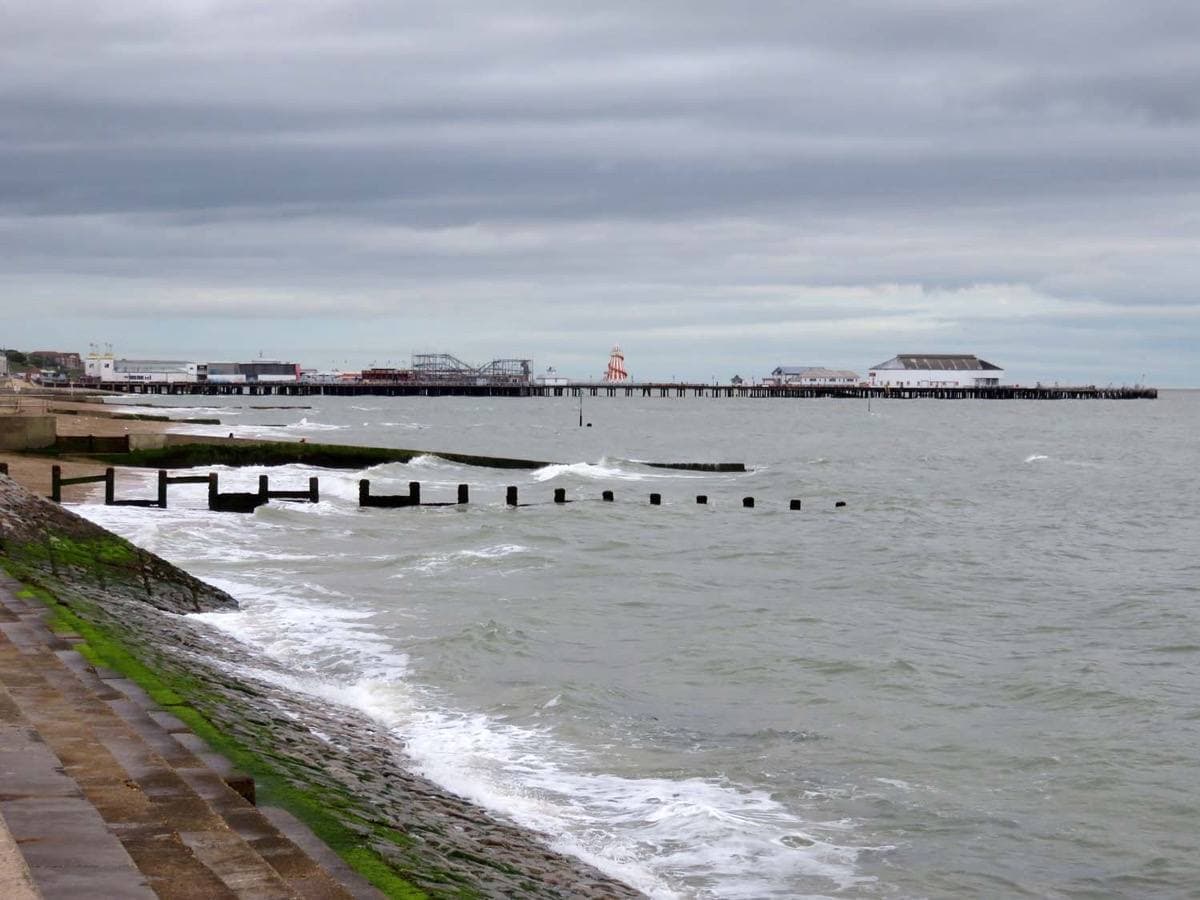 Clacton Pier stretching out over a grey sea, waves breaking on the sea wall