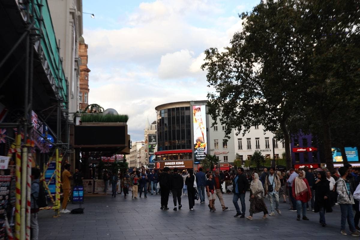 Crowds walking through Leicester Square under the trees