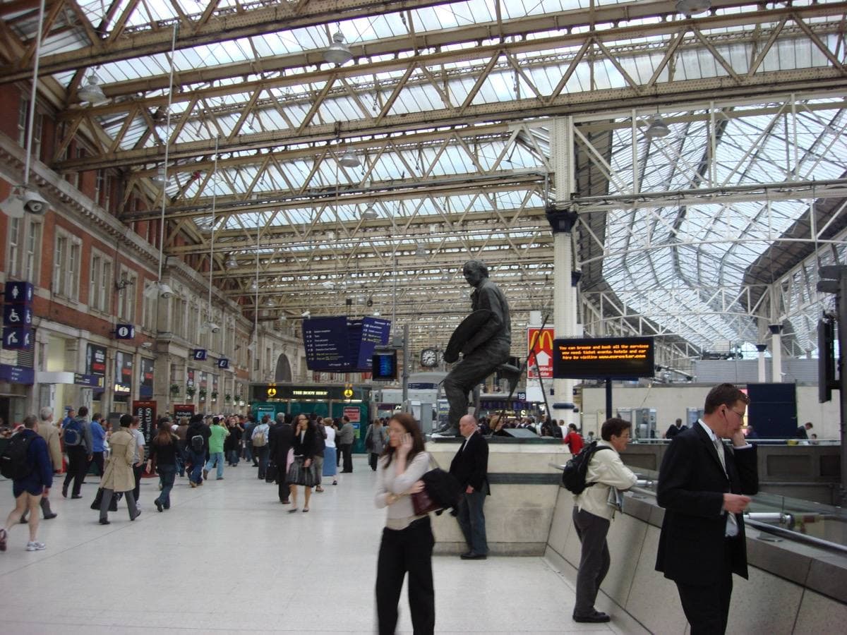The glass-roofed concourse at Waterloo station with travellers walking under the departure boards