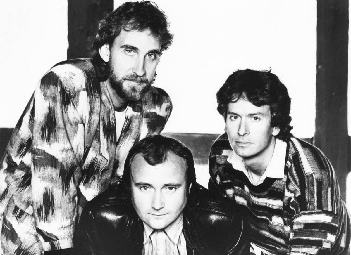 Black-and-white photograph of three men in patterned jackets, Phil Collins in front