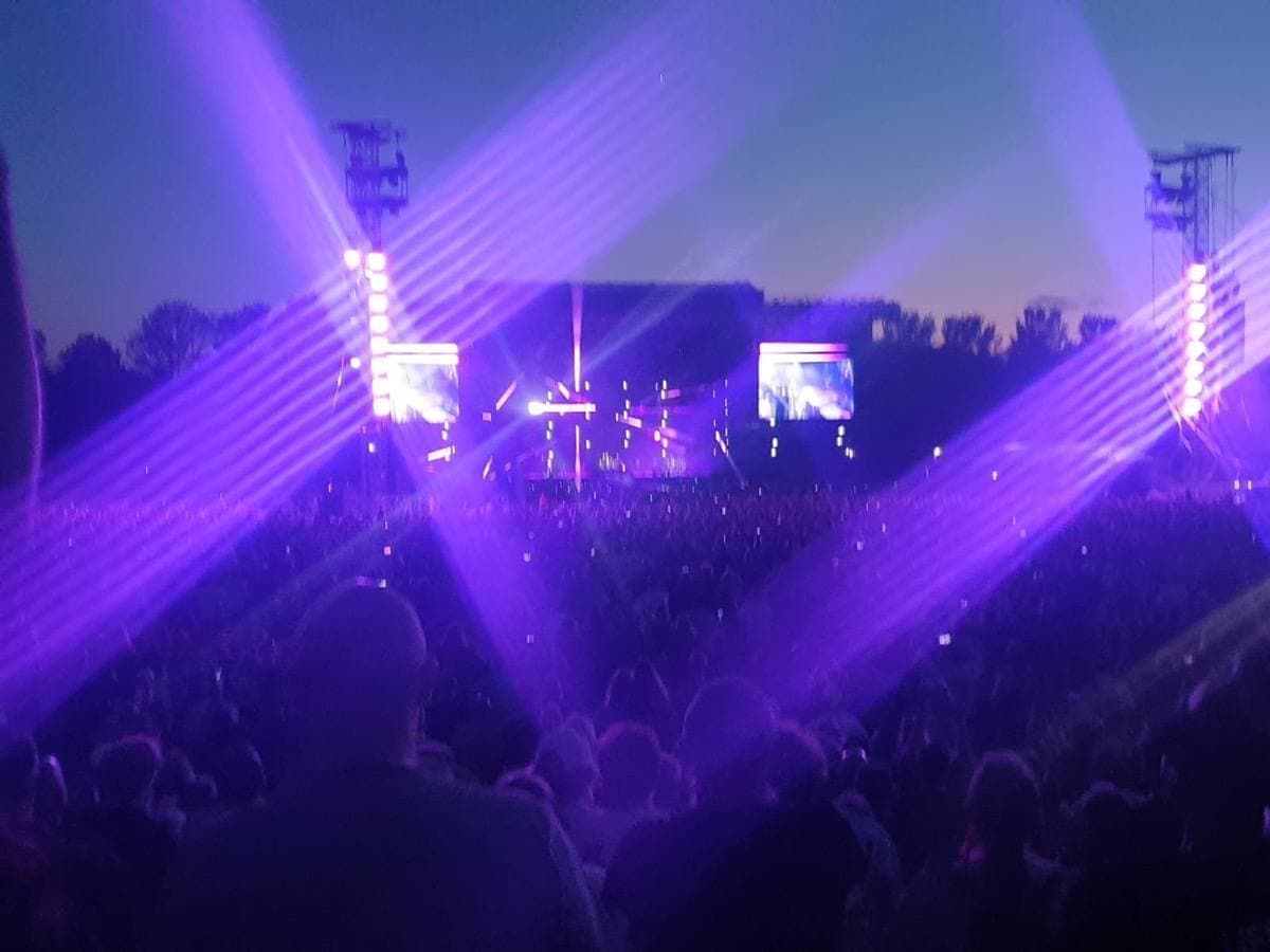 Purple lights over a crowd at an outdoor stage at dusk