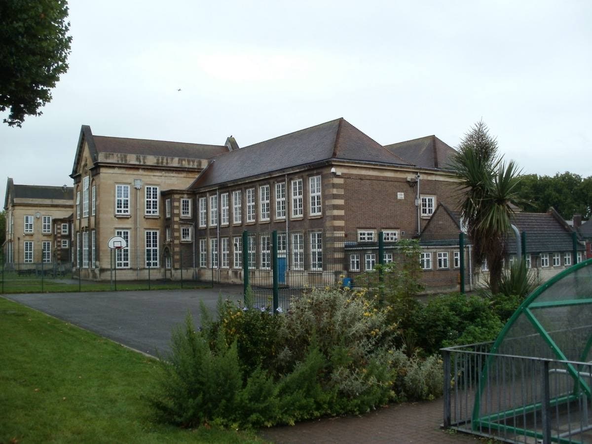 A brick school building with tall windows behind a garden on Burlington Lane