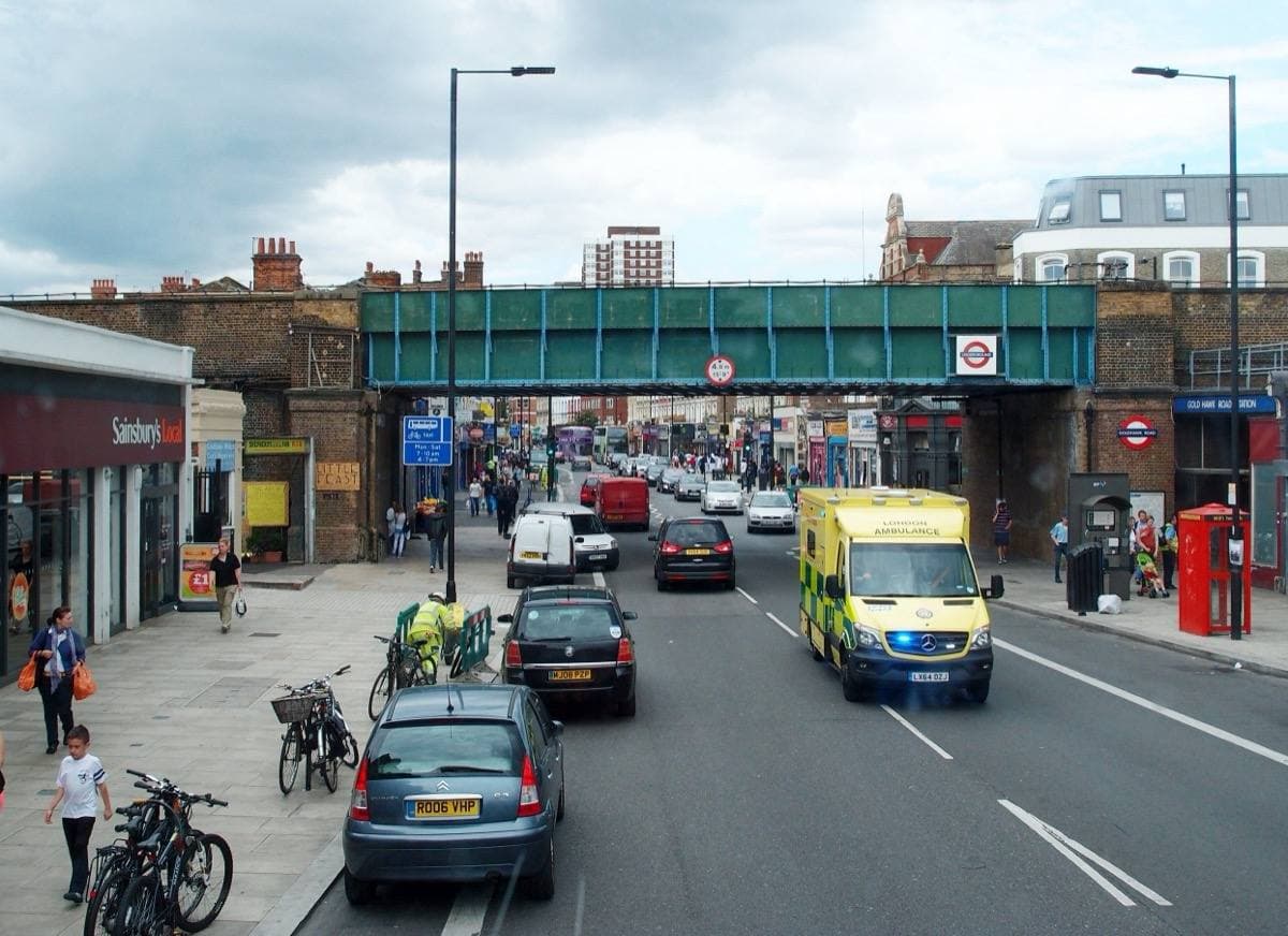 A busy stretch of Goldhawk Road with traffic under a railway bridge