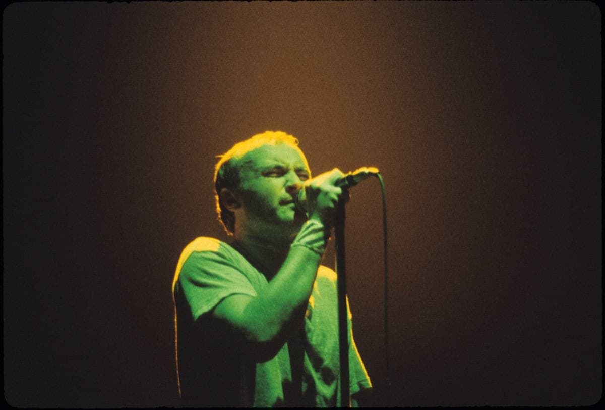 Phil Collins singing in a pool of green light on a dark stage
