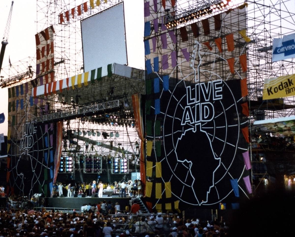The Live Aid stage in Philadelphia by day, scaffolding and the Live Aid globe logo above a crowd