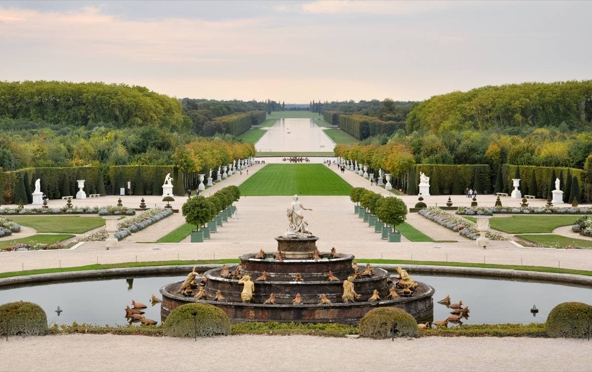 A long garden vista with a fountain basin, clipped hedges and a green avenue