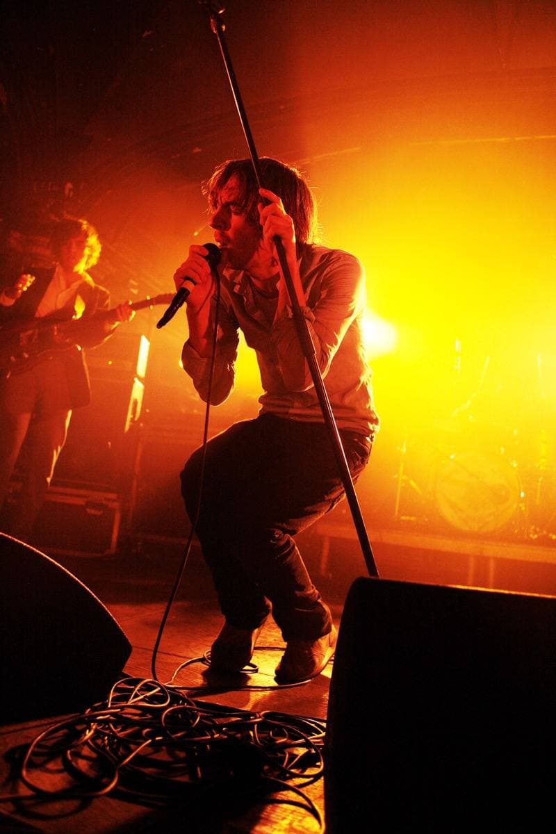 Thomas Mars singing into a microphone on a stand, lit orange from behind