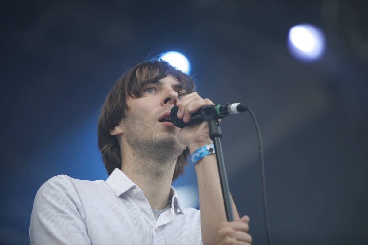 Thomas Mars in a white shirt singing into a microphone, a blue spotlight behind