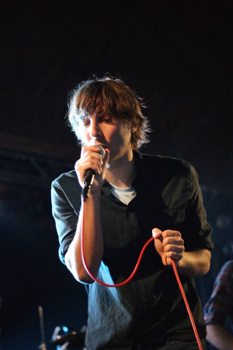 Thomas Mars in a dark shirt holding a microphone with a red cable