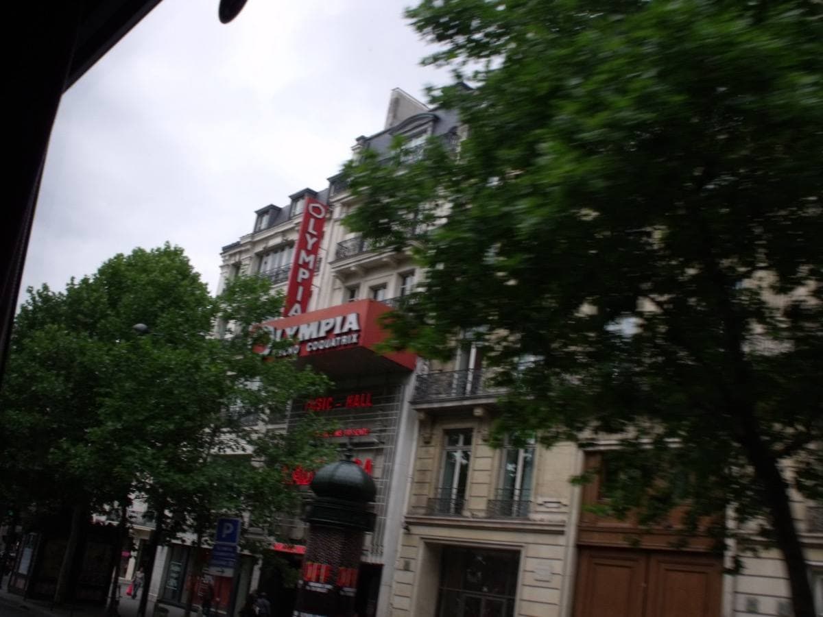 A red-lettered music-hall sign on a Paris boulevard behind trees