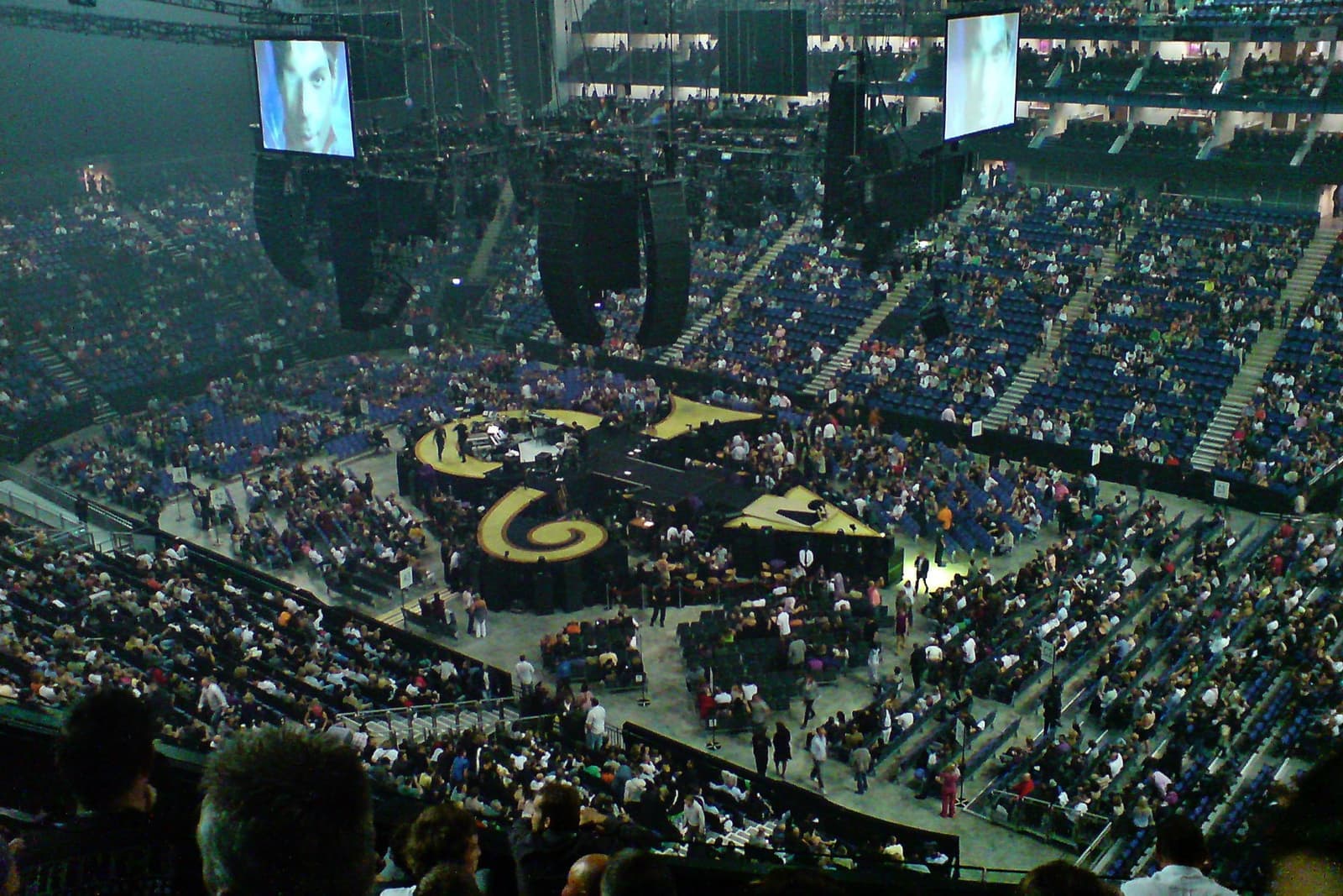 A packed arena around a lit stage in the middle of the floor