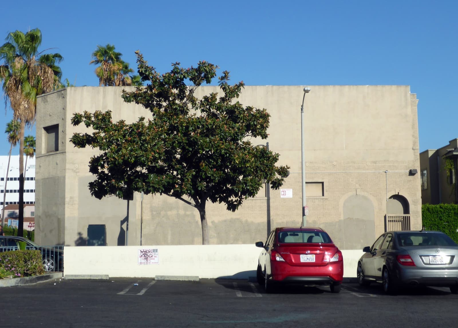 A plain cream studio building with a tree and parked cars
