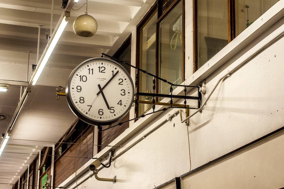 A round clock hanging from a bracket inside Castle Market on its last day, under strip lights