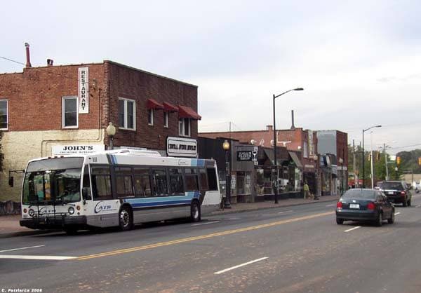 A city avenue with a bus, low brick shops and street lights