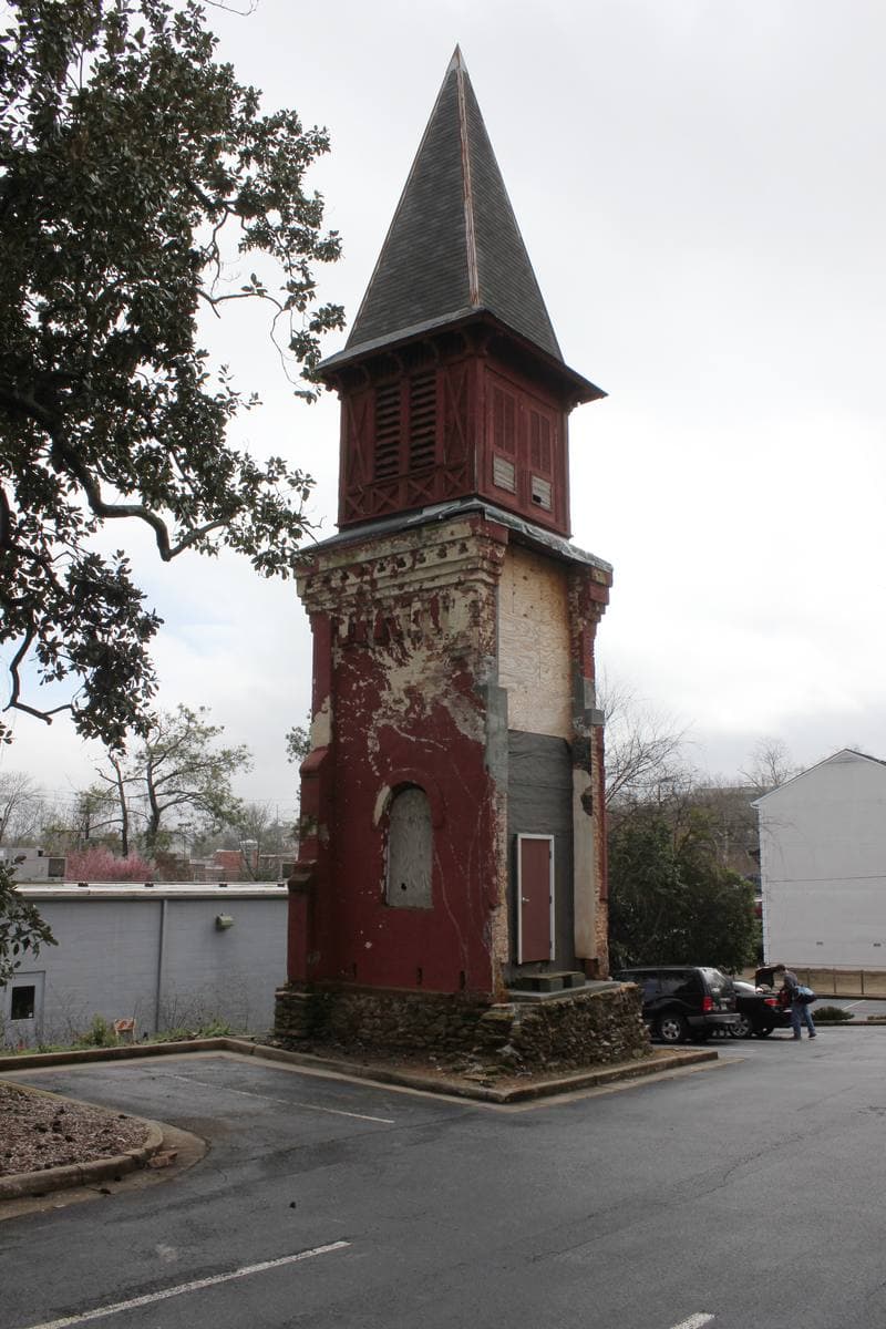 A lone red-brick steeple with a dark pointed roof standing at the edge of a car park