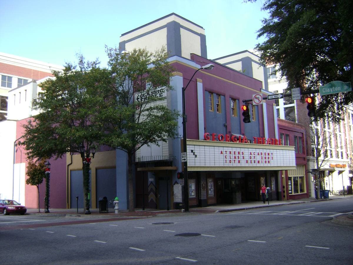 A tall theatre front with a marquee on a street corner, trees in front