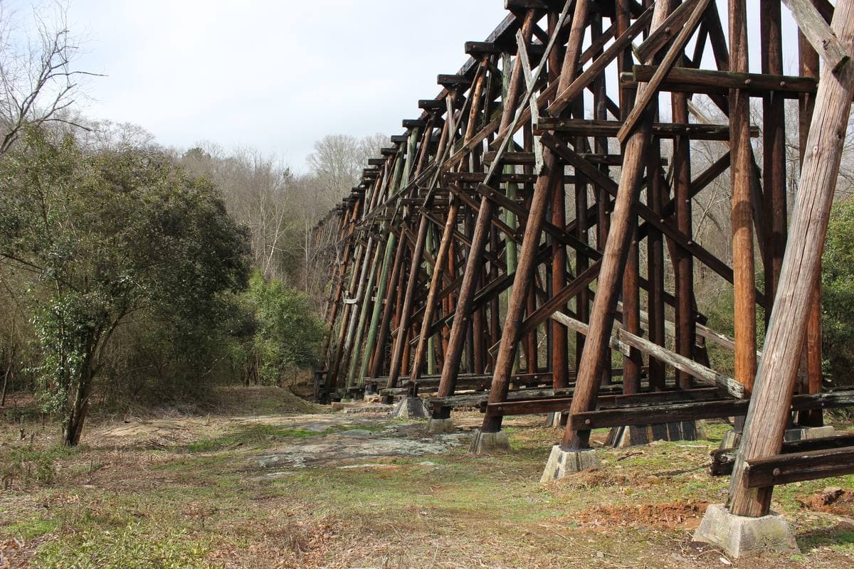 A long weathered timber railway trestle crossing a grassy valley