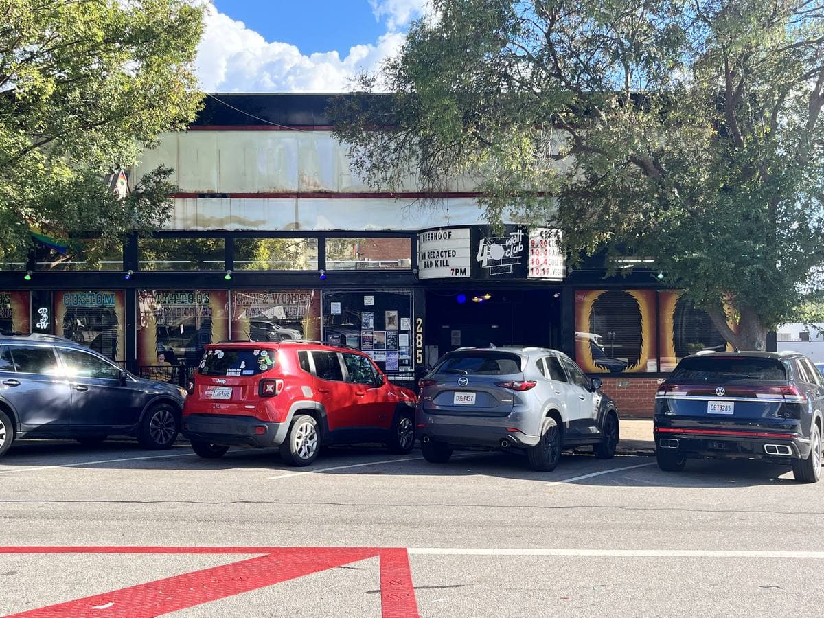A low club front with a canopy and posters, cars parked in front