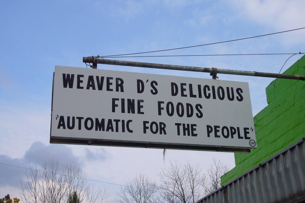 A white hanging sign in black capitals: Weaver D’s Delicious Fine Foods, Automatic for the People