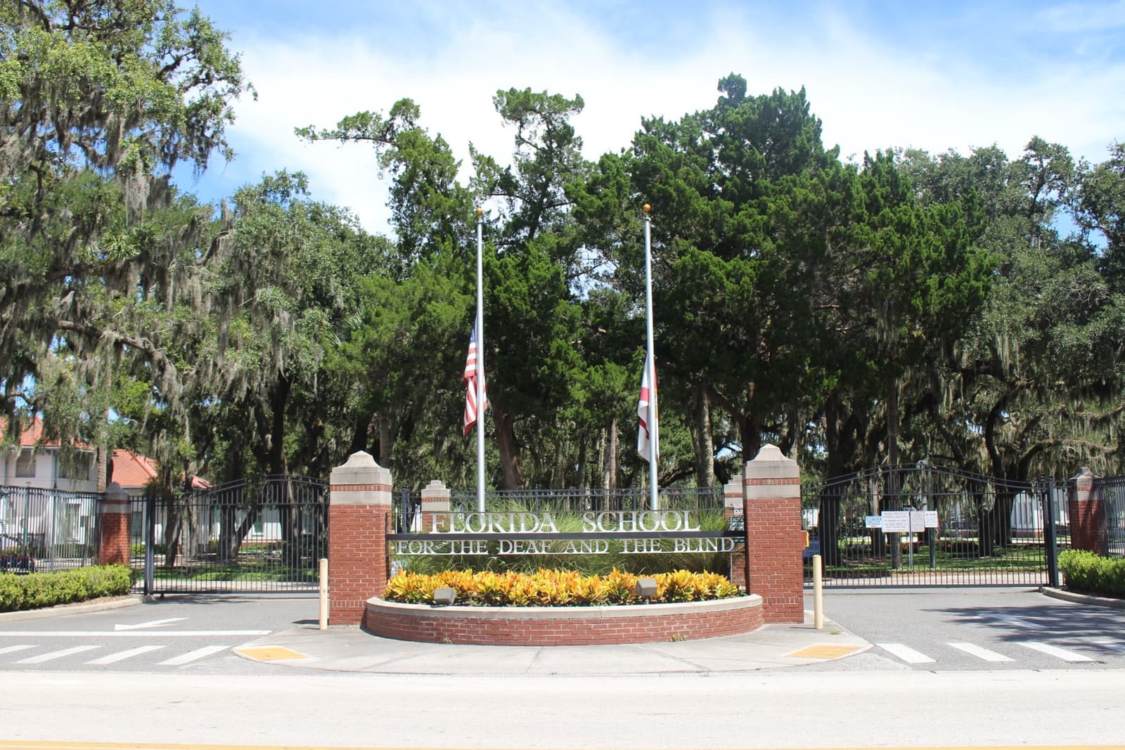 Brick gate pillars and a curved sign for the Florida School for the Deaf and the Blind, oaks and flags behind