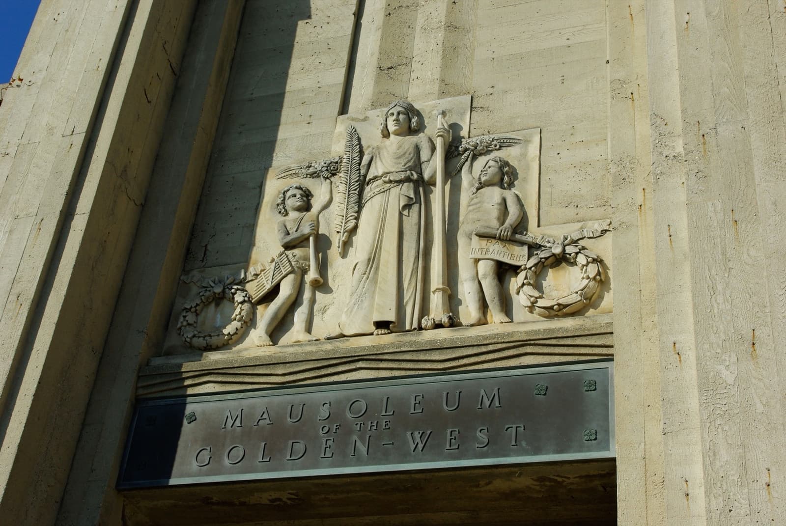 A carved stone relief of three figures above a bronze plaque reading Mausoleum of the Golden West