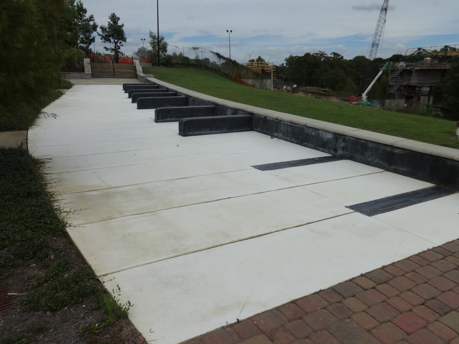 A pale concrete path laid out with black stripes like piano keys, leading down through grass