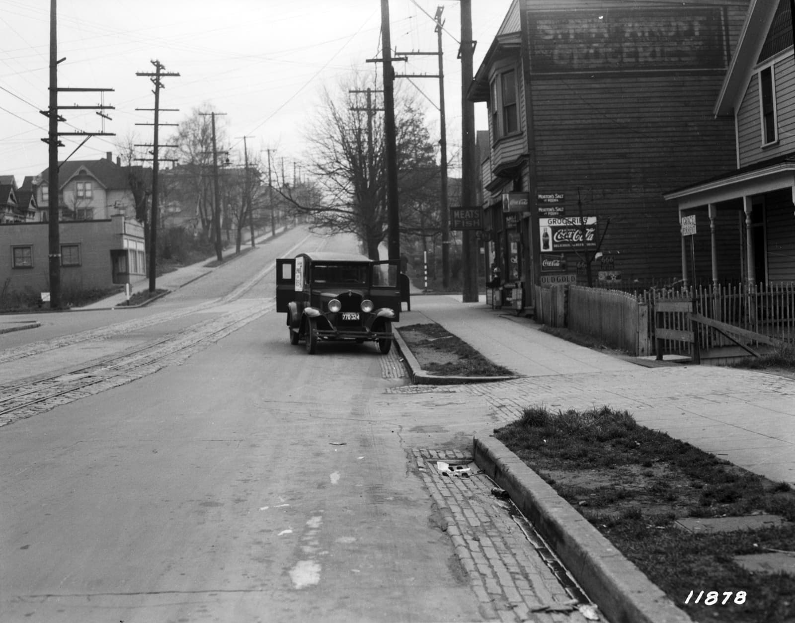Black-and-white view of a wide street with wooden buildings, poles and a parked truck