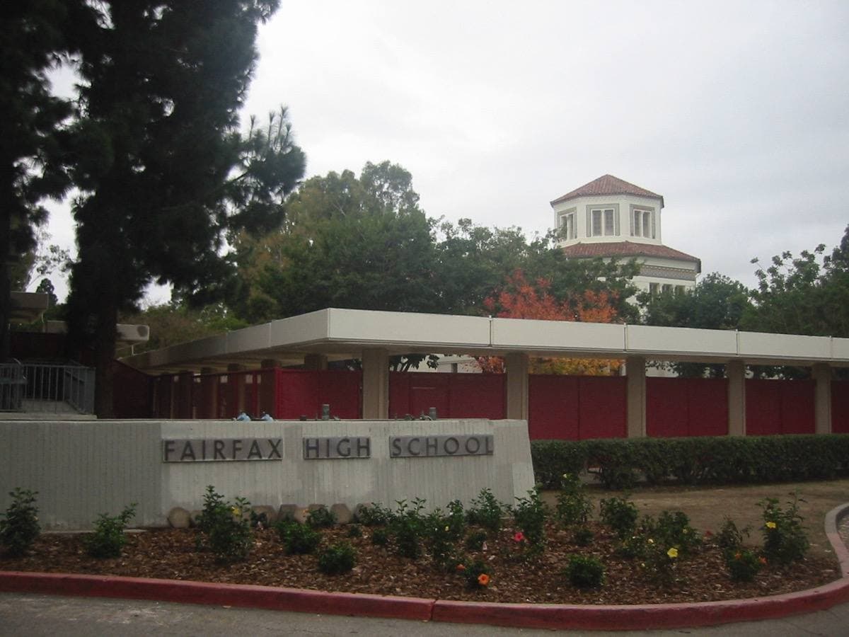 The front of Fairfax High School, a pale building behind lawns and palm trees
