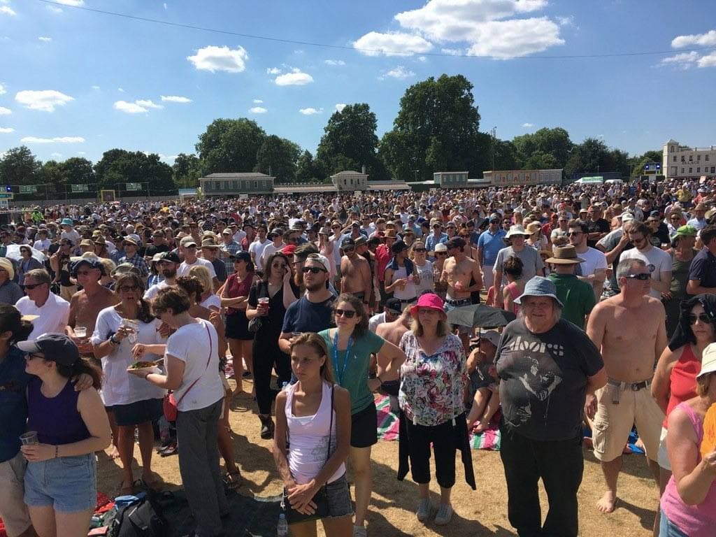 A large crowd on the grass in front of a distant stage