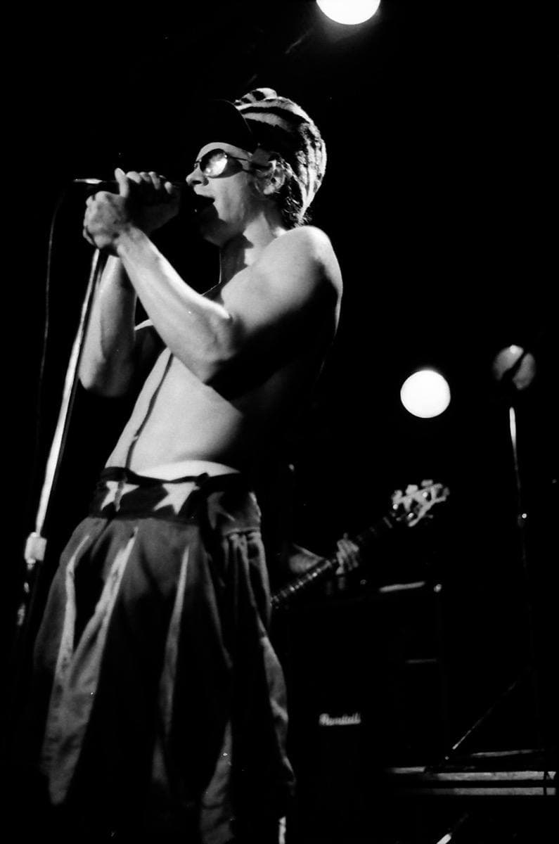 Anthony Kiedis singing into a microphone in dark glasses and a striped cap, 1985
