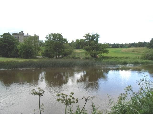 A castle above trees and a green slope beyond a slow river