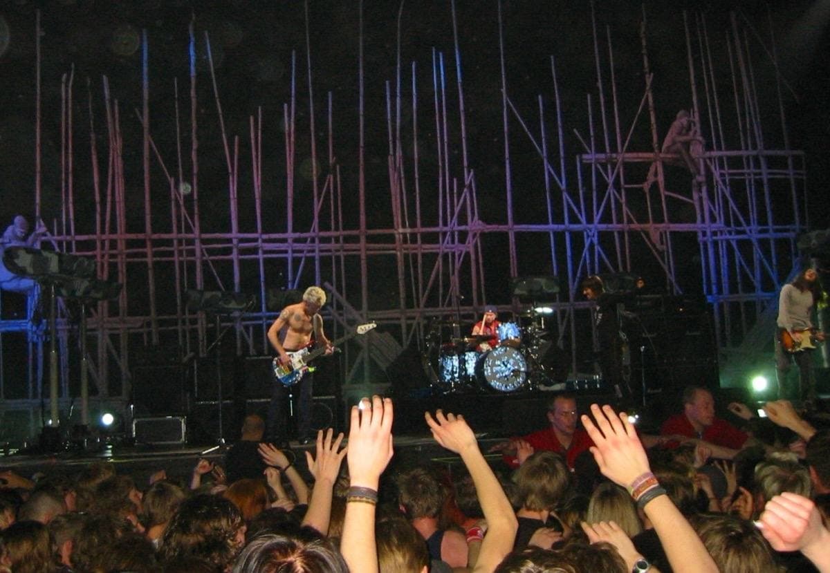 A concert stage lit blue and pink above a crowd with raised hands