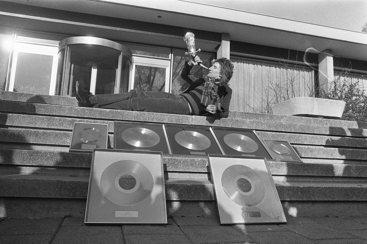 Rod Stewart lying on the top of the hotel steps above a row of framed gold records