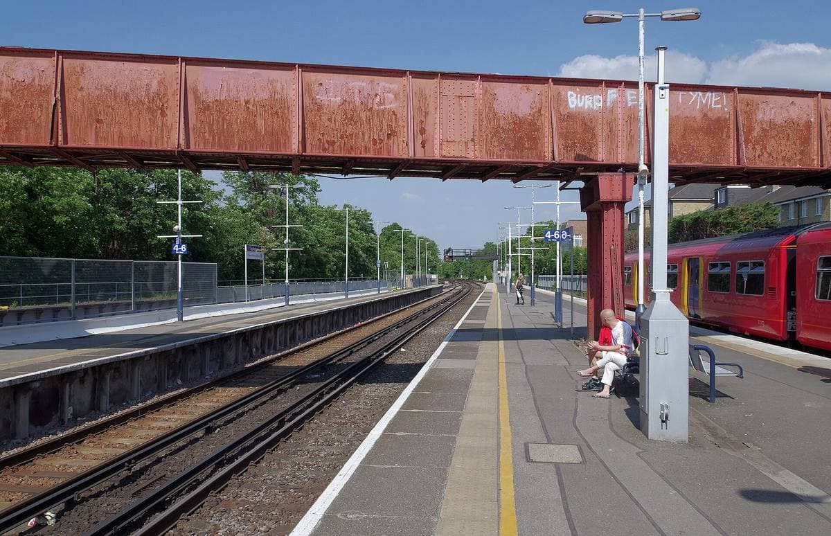 A long platform under a red footbridge, with a red train at the far end