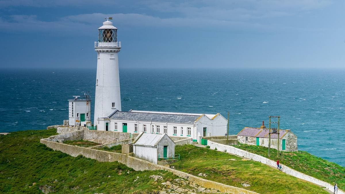 A white lighthouse and keepers’ buildings on a green island above a blue sea