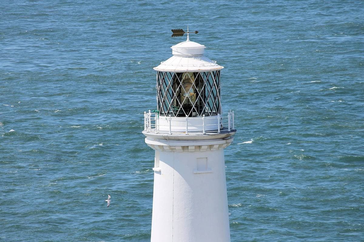 A white lighthouse tower seen from above against the sea