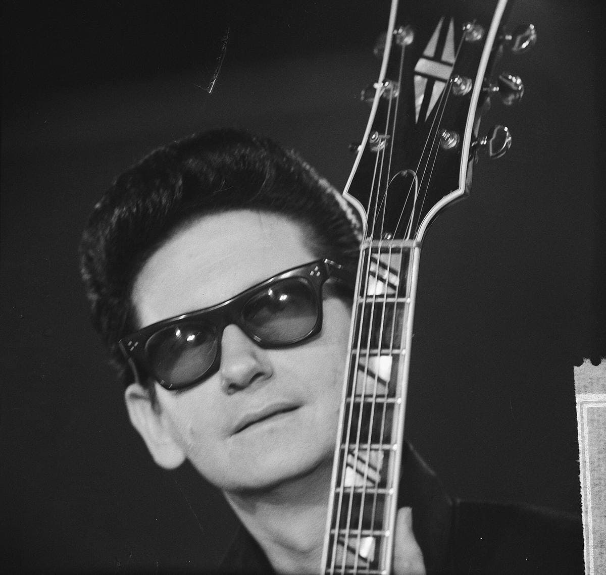 Roy Orbison in dark glasses beside the headstock of his guitar