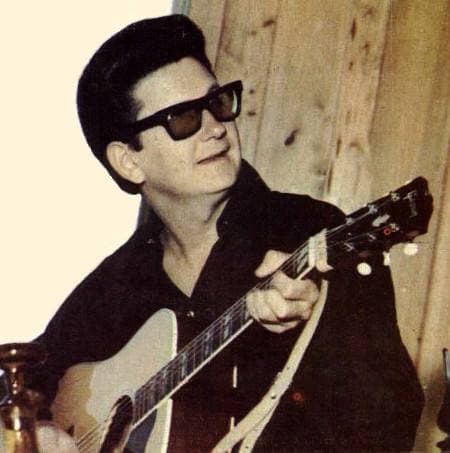 Roy Orbison in dark glasses with an acoustic guitar against wooden boards