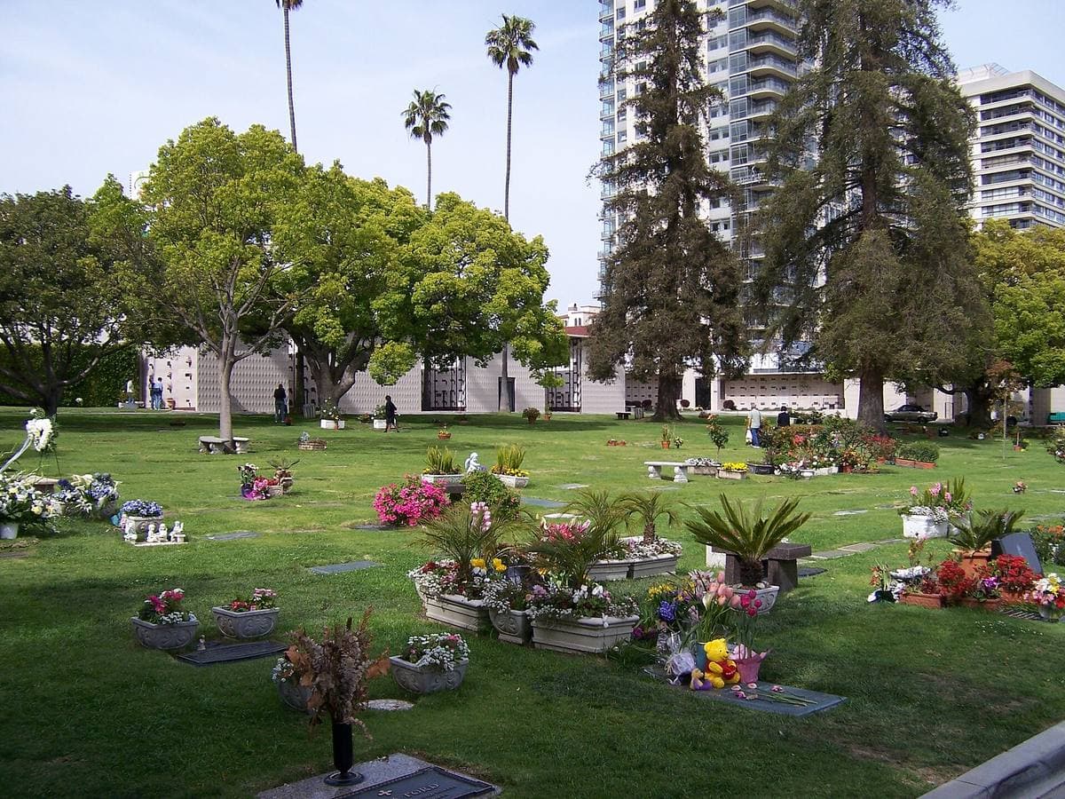 A small lawn cemetery with flowers on flat markers, office towers behind