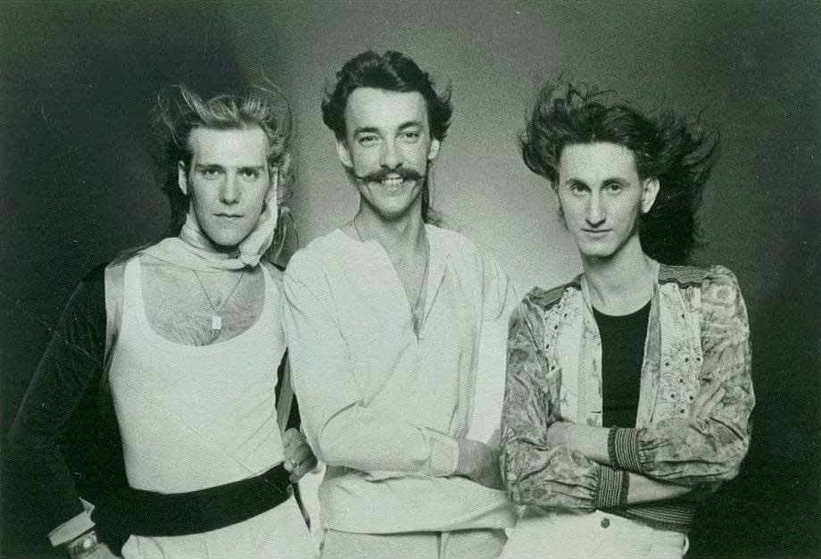 Alex Lifeson, Neil Peart and Geddy Lee in 1976, hair blown back, in white and patterned shirts
