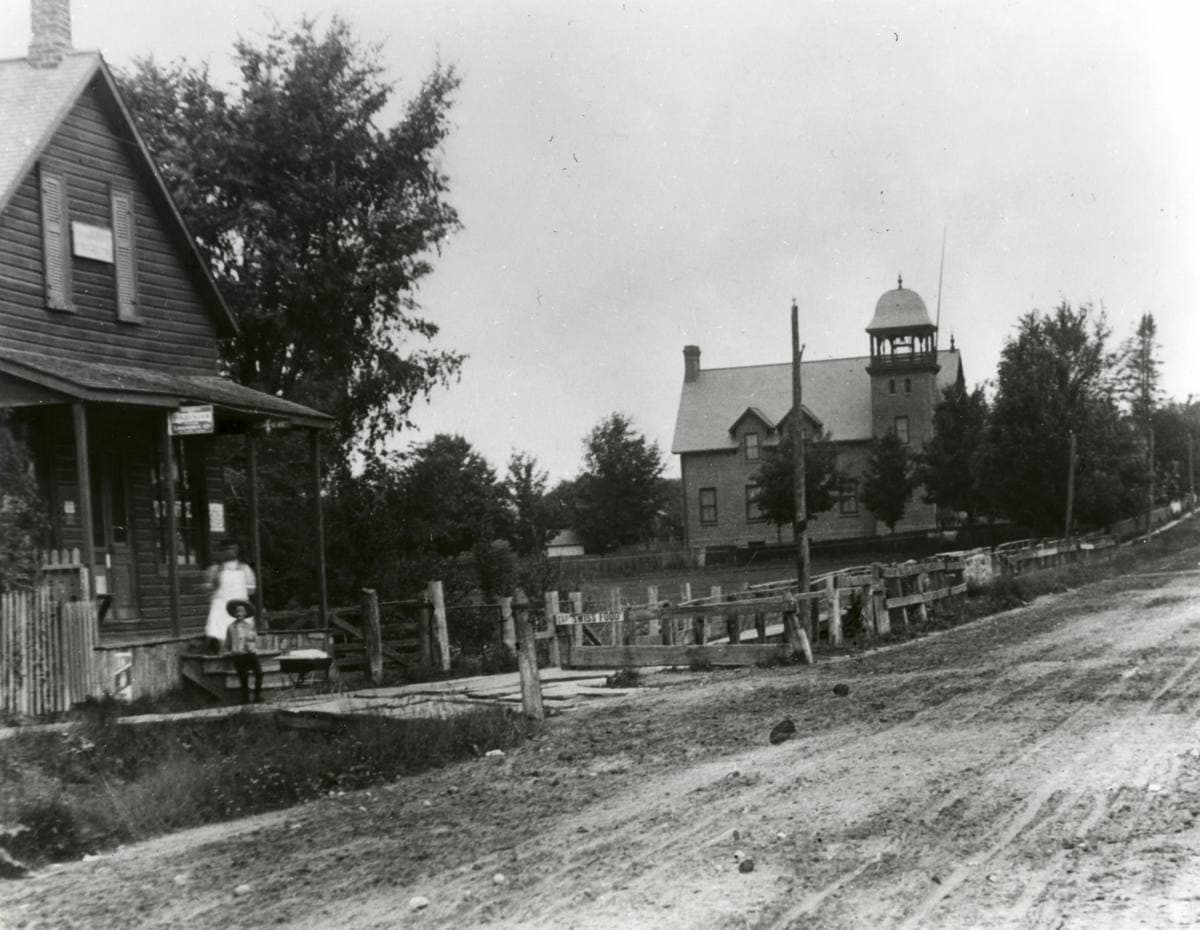An old photograph of a country road with a wooden store and a school