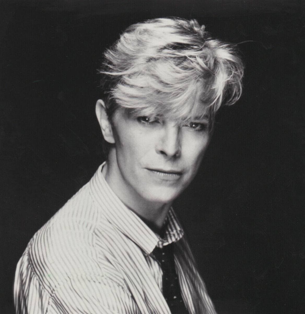 David Bowie in a striped shirt and knitted tie, looking over his shoulder, black and white